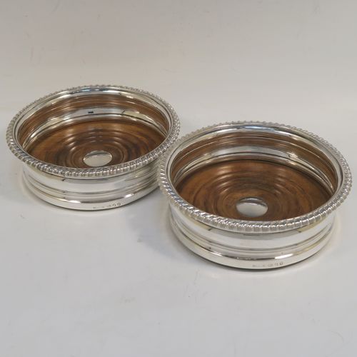 A very handsome pair of Antique Georgian Sterling Silver wine bottle table coasters, in a Georgian Regency style, having round bellied bodies with applied gadroon borders, and oak wood-turned bases with silver buttons. These elegant antique silver wine coasters were made by John and Thomas Settle of Sheffield in 1816. The dimensions of these fine hand-made antique silver wine bottle coasters are diameter 14.5 cms (5.75 inches), and height 4.5 cms (1.75 inches).  