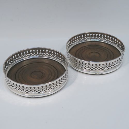 A very elegant Sterling Silver pair of Neoclassical style wine coasters, having hand-pierced and engraved walls, with plain oak turned bases. These beautiful silver bottle coasters were made by DaMar Silverware of London in 1975. The dimensions of this fine hand-made pair of silver wine bottle coasters are diameter 13 cms (5 inches), and height 3 cms (1.25 inches).   