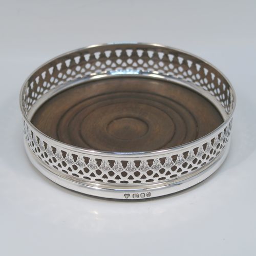 A very elegant Sterling Silver pair of Neoclassical style wine coasters, having hand-pierced and engraved walls, with plain oak turned bases. These beautiful silver bottle coasters were made by DaMar Silverware of London in 1975. The dimensions of this fine hand-made pair of silver wine bottle coasters are diameter 13 cms (5 inches), and height 3 cms (1.25 inches).