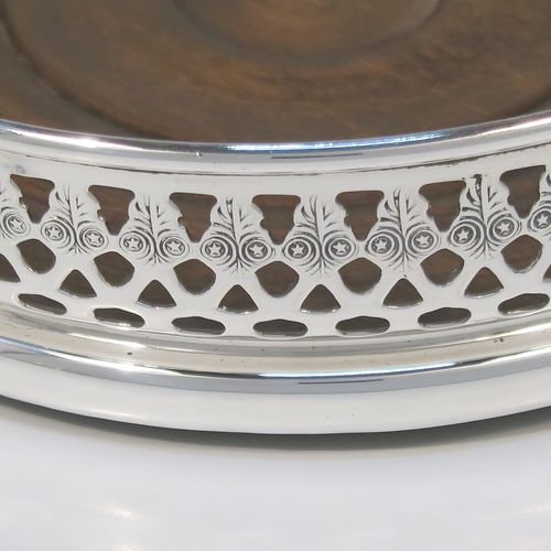 A very elegant Sterling Silver pair of Neoclassical style wine coasters, having hand-pierced and engraved walls, with plain oak turned bases. These beautiful silver bottle coasters were made by DaMar Silverware of London in 1975. The dimensions of this fine hand-made pair of silver wine bottle coasters are diameter 13 cms (5 inches), and height 3 cms (1.25 inches).