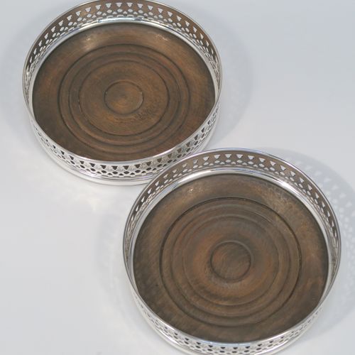 A very elegant Sterling Silver pair of Neoclassical style wine coasters, having hand-pierced and engraved walls, with plain oak turned bases. These beautiful silver bottle coasters were made by DaMar Silverware of London in 1975. The dimensions of this fine hand-made pair of silver wine bottle coasters are diameter 13 cms (5 inches), and height 3 cms (1.25 inches).