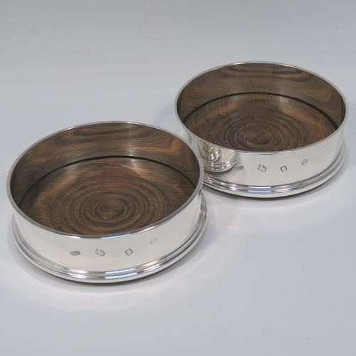 A very elegant pair of Sterling Silver table wine bottle coasters, having plain round straight sided bodies, with applied reeded top borders, and stained fruit wood turned bases. This handsome pair of silver wine bottle coasters were made by Richard Knight of London in 1970. The dimensions of these fine hand-made silver wine coasters are diameter 12.5 cms (5 inches), and height 4 cms (1.5 inches).   
