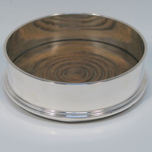 A very elegant pair of Sterling Silver table wine bottle coasters, having plain round straight sided bodies, with applied reeded top borders, and stained fruit wood turned bases. This handsome pair of silver wine bottle coasters were made by Richard Knight of London in 1970. The dimensions of these fine hand-made silver wine coasters are diameter 12.5 cms (5 inches), and height 4 cms (1.5 inches).