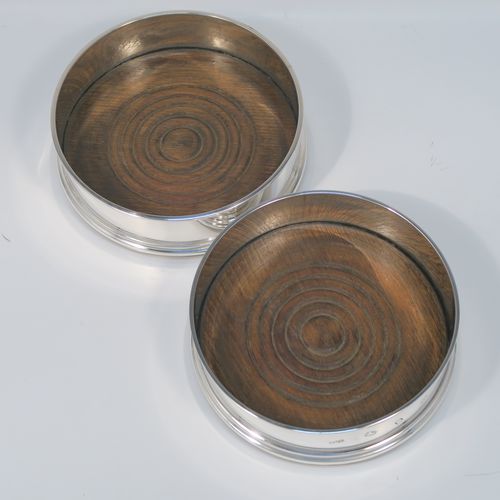 A very elegant pair of Sterling Silver table wine bottle coasters, having plain round straight sided bodies, with applied reeded top borders, and stained fruit wood turned bases. This handsome pair of silver wine bottle coasters were made by Richard Knight of London in 1970. The dimensions of these fine hand-made silver wine coasters are diameter 12.5 cms (5 inches), and height 4 cms (1.5 inches).