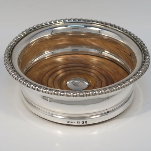 A very handsome pair of Antique Georgian Sterling Silver wine bottle table coasters, in a Georgian Regency style, having round bellied bodies with applied gadroon borders, and oak wood-turned bases with silver buttons. These elegant antique silver wine coasters were made by John and Thomas Settle of Sheffield in 1821. The dimensions of these fine hand-made antique silver wine bottle coasters are diameter 16 cms (6.3 inches), and height 5 cms (2 inches). Please note that the silver buttons are part-crested.