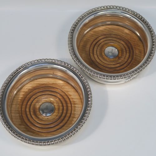 A very handsome pair of Antique Georgian Sterling Silver wine bottle table coasters, in a Georgian Regency style, having round bellied bodies with applied gadroon borders, and oak wood-turned bases with silver buttons. These elegant antique silver wine coasters were made by John and Thomas Settle of Sheffield in 1821. The dimensions of these fine hand-made antique silver wine bottle coasters are diameter 16 cms (6.3 inches), and height 5 cms (2 inches). Please note that the silver buttons are part-crested.