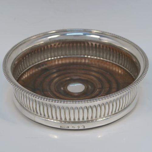 A very handsome Antique Georgian Sterling Silver wine bottle table coaster, in a Regency style, having a round bellied body with a hand-chased melon vertical fluting, an applied gadroon border, and an oak wood-turned base with central silver button. This elegant silver bottle coaster was made by John Roberts of Sheffield in 1806. The dimensions of this fine hand-made antique silver wine bottle coaster are diameter 14.5 cms (5.75 inches), and height 4 cms (1.5 inches).   