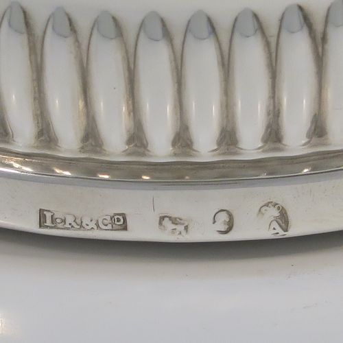 A very handsome Antique Georgian Sterling Silver wine bottle table coaster, in a Regency style, having a round bellied body with a hand-chased melon vertical fluting, an applied gadroon border, and an oak wood-turned base with central silver button. This elegant silver bottle coaster was made by John Roberts of Sheffield in 1806. The dimensions of this fine hand-made antique silver wine bottle coaster are diameter 14.5 cms (5.75 inches), and height 4 cms (1.5 inches).