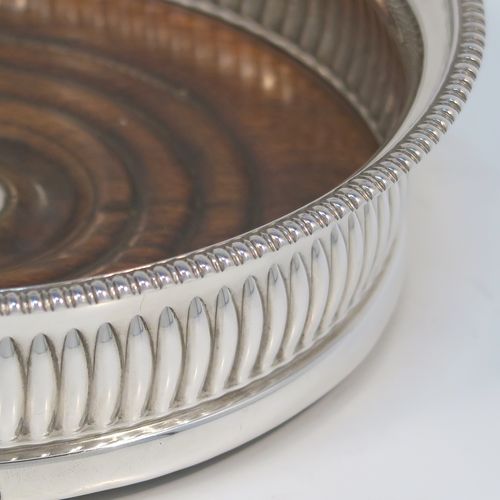 A very handsome Antique Georgian Sterling Silver wine bottle table coaster, in a Regency style, having a round bellied body with a hand-chased melon vertical fluting, an applied gadroon border, and an oak wood-turned base with central silver button. This elegant silver bottle coaster was made by John Roberts of Sheffield in 1806. The dimensions of this fine hand-made antique silver wine bottle coaster are diameter 14.5 cms (5.75 inches), and height 4 cms (1.5 inches).