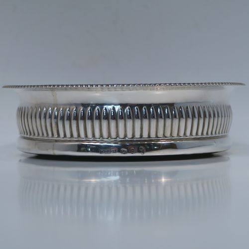 A very handsome Antique Georgian Sterling Silver wine bottle table coaster, in a Regency style, having a round bellied body with a hand-chased melon vertical fluting, an applied gadroon border, and an oak wood-turned base with central silver button. This elegant silver bottle coaster was made by John Roberts of Sheffield in 1806. The dimensions of this fine hand-made antique silver wine bottle coaster are diameter 14.5 cms (5.75 inches), and height 4 cms (1.5 inches).