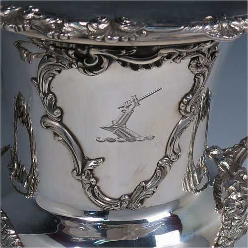 An Antique Georgian Old Sheffield plated wine cooler, in the Campagna style, with cast floral borders, a pair of cast anthemion leaf handles, and applied scroll cartouches either side. All with original interior and cover. Made in ca. 1835. The dimensions of this fine hand-made antique Old Sheffield plated wine cooler are height 30.5 cms (12 inches), width across handles 26 cms (10.25inches). Please note that this item is crested on one side.