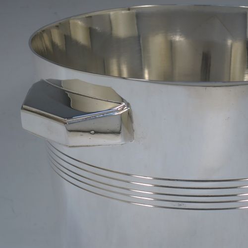 A very handsome Art Deco style Silver Plated wine bottle cooler, having a plain round body with tapering sides, with two cast angular side-handles, and two bands of hand-chased reeded decoration, all sitting on a flat base. Made in ca. 1930. The dimensions of this fine hand-made silver-plated wine cooler are height 21 cms (8.25 inches), and diameter at lip 18.5 cms (7.25 inches). Please note that this will easily hold a magnum size bottle.