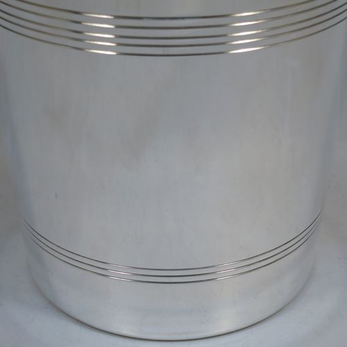 A very handsome Art Deco style Silver Plated wine bottle cooler, having a plain round body with tapering sides, with two cast angular side-handles, and two bands of hand-chased reeded decoration, all sitting on a flat base. Made in ca. 1930. The dimensions of this fine hand-made silver-plated wine cooler are height 21 cms (8.25 inches), and diameter at lip 18.5 cms (7.25 inches). Please note that this will easily hold a magnum size bottle.