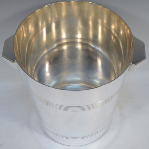 A very handsome Art Deco style Silver Plated wine bottle cooler, having a plain round body with tapering sides, with two cast angular side-handles, and two bands of hand-chased reeded decoration, all sitting on a flat base. Made in ca. 1930. The dimensions of this fine hand-made silver-plated wine cooler are height 21 cms (8.25 inches), and diameter at lip 18.5 cms (7.25 inches). Please note that this will easily hold a magnum size bottle.