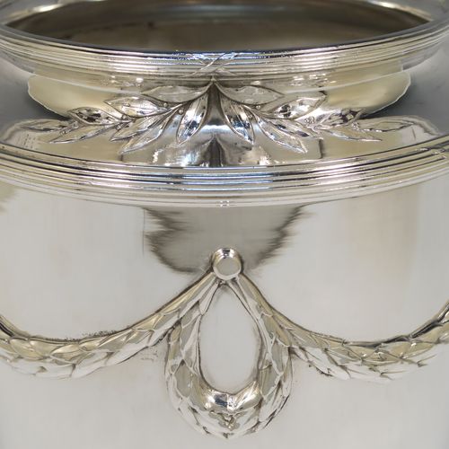 A very elegant Neoclassical style Antique Victorian silver-plated wine cooler, having a plain round body with tapering sides, with beautiful applied acanthus leaf swags, two cast scroll side-handles, and all sitting on a pedestal foot. This handsome antique silver plated wine bottle cooler was made in ca. 1880. The dimensions of this fine hand-made antique silver wine cooler are height 24 cms (9.5 inches), width across handles 25.5 cms (10 inches).