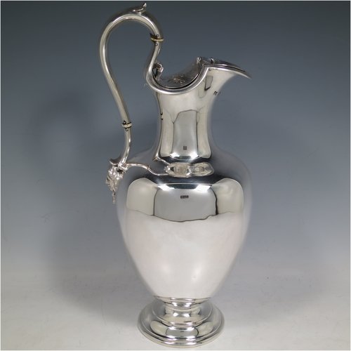 An Antique Victorian Sterling Silver wine ewer, having a plain round baluster body, an insulated scroll handle, a hinged lid with with floral finial over a shaped spout, and all sitting on a round pedestal foot. Made by the Barnard Brothers of London in 1850. The dimensions of this fine hand-made antique sterling silver wine ewer are height 32 cms (12.5 inches), length 14 cms (5.5 inches), and it weighs approx. 790g (25.5 troy ounces).