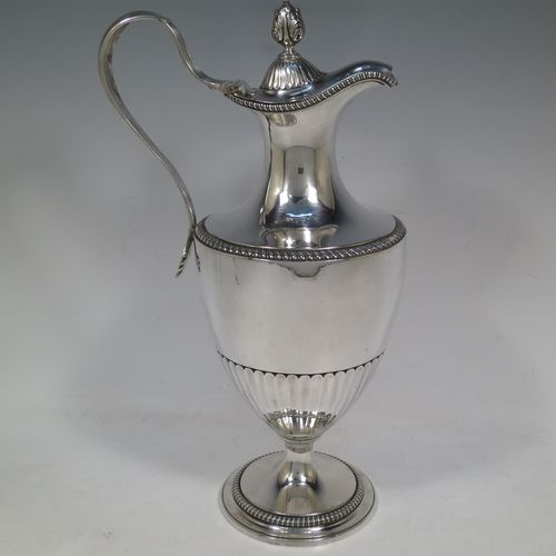 A very handsome and rare Antique Georgian Sterling Silver wine ewer, having an amphora style round bellied body, with applied gadroon borders and hand-chased half-fluted decoration, a hinged lid with cast anthemion leaf finial and a classical scroll handle, and all sitting on a pedestal foot. Made by Daniel Smith and Robert Sharp of London in 1784. The dimensions of this fine hand-made antique silver wine ewer are height 31 cms (12.25 inches), length 17 cms (6.75 inches), and it weighs approx. 840g (27 troy ounces).