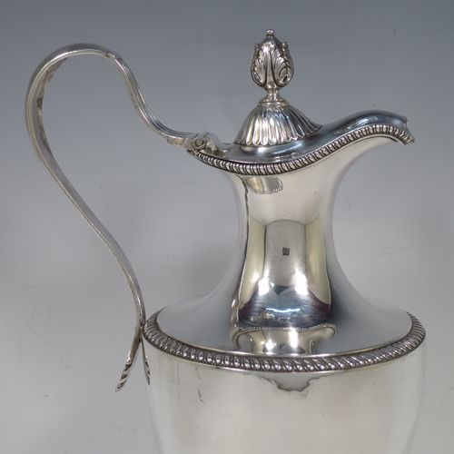 A very handsome and rare Antique Georgian Sterling Silver wine ewer, having an amphora style round bellied body, with applied gadroon borders and hand-chased half-fluted decoration, a hinged lid with cast anthemion leaf finial and a classical scroll handle, and all sitting on a pedestal foot. Made by Daniel Smith and Robert Sharp of London in 1784. The dimensions of this fine hand-made antique silver wine ewer are height 31 cms (12.25 inches), length 17 cms (6.75 inches), and it weighs approx. 840g (27 troy ounces).