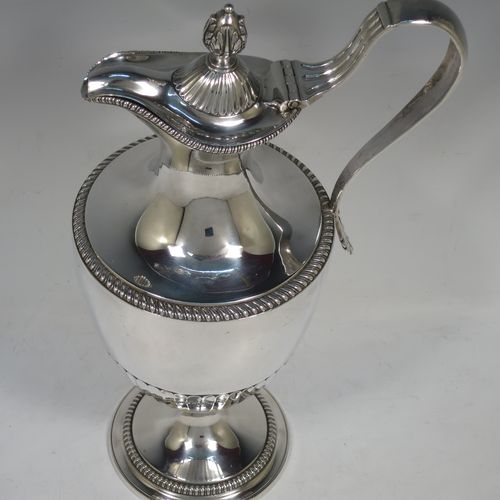 A very handsome and rare Antique Georgian Sterling Silver wine ewer, having an amphora style round bellied body, with applied gadroon borders and hand-chased half-fluted decoration, a hinged lid with cast anthemion leaf finial and a classical scroll handle, and all sitting on a pedestal foot. Made by Daniel Smith and Robert Sharp of London in 1784. The dimensions of this fine hand-made antique silver wine ewer are height 31 cms (12.25 inches), length 17 cms (6.75 inches), and it weighs approx. 840g (27 troy ounces).