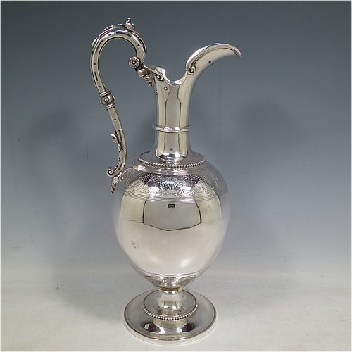 An Antique Victorian Sterling Silver wine ewer, having an amphora style round bellied body, with a band of hand-engraved floral decoration, together with applied bead borders, a lid with flat invisible hinge, a scroll handle with thumb-piece, and all sitting on a pedestal foot. Made by Arthur Sibley of London in 1869. The dimensions of this fine hand-made antique silver wine ewer are height 34 cms (13.3 inches), length 16 cms (6.25 inches), and it weighs approx. 848g (27 troy ounces).