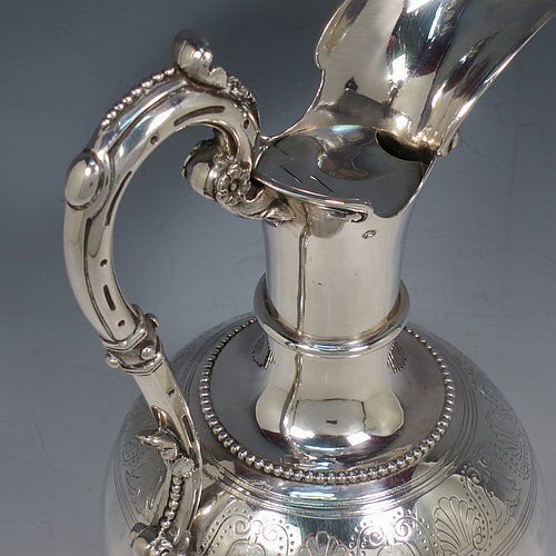 An Antique Victorian Sterling Silver wine ewer, having an amphora style round bellied body, with a band of hand-engraved floral decoration, together with applied bead borders, a lid with flat invisible hinge, a scroll handle with thumb-piece, and all sitting on a pedestal foot. Made by Arthur Sibley of London in 1869. The dimensions of this fine hand-made antique silver wine ewer are height 34 cms (13.3 inches), length 16 cms (6.25 inches), and it weighs approx. 848g (27 troy ounces).