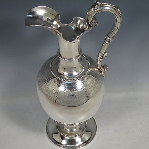 An Antique Victorian Sterling Silver wine ewer, having an amphora style round bellied body, with a band of hand-engraved floral decoration, together with applied bead borders, a lid with flat invisible hinge, a scroll handle with thumb-piece, and all sitting on a pedestal foot. Made by Arthur Sibley of London in 1869. The dimensions of this fine hand-made antique silver wine ewer are height 34 cms (13.3 inches), length 16 cms (6.25 inches), and it weighs approx. 848g (27 troy ounces).