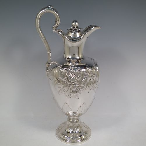 A beautiful Antique Victorian Sterling Silver wine ewer, having an amphora style round bellied body, with hand-chased floral and scroll decoration, a hinged lid with cast finial, an insulated scroll handle, and all sitting on a pedestal foot. This handsome antique silver ewer was made by the Barnard Brothers of London in 1849. The dimensions of this fine hand-made antique silver wine ewer are height 35 cms (13.5 inches), length 16.5 cms (6.5 inches), and it weighs approx. 868g (28 troy ounces).