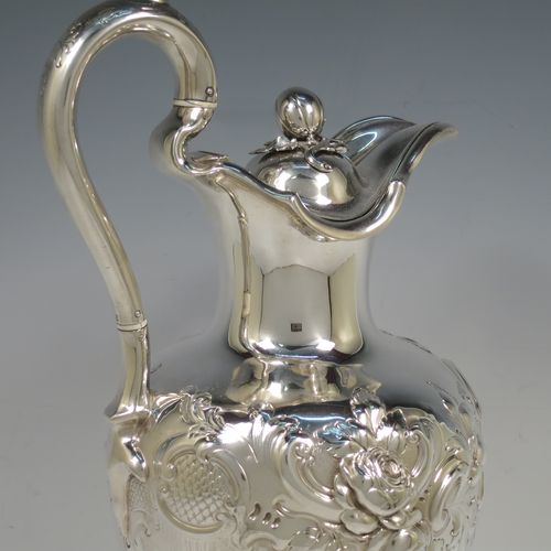A beautiful Antique Victorian Sterling Silver wine ewer, having an amphora style round bellied body, with hand-chased floral and scroll decoration, a hinged lid with cast finial, an insulated scroll handle, and all sitting on a pedestal foot. This handsome antique silver ewer was made by the Barnard Brothers of London in 1849. The dimensions of this fine hand-made antique silver wine ewer are height 35 cms (13.5 inches), length 16.5 cms (6.5 inches), and it weighs approx. 868g (28 troy ounces).